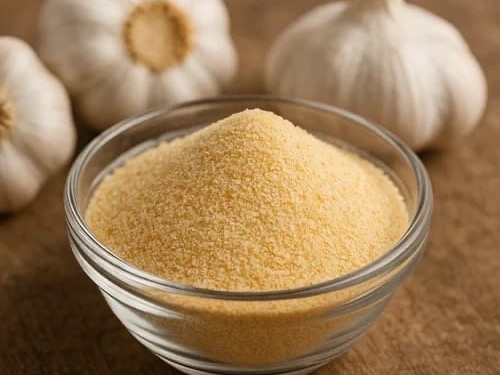 Golden garlic powder in a glass bowl with whole garlic bulbs