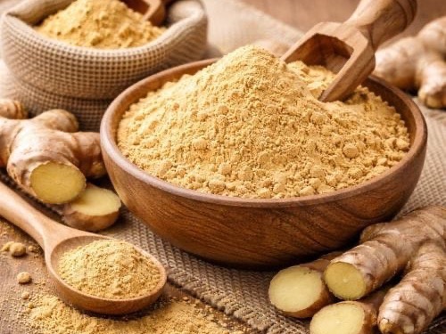 Ginger powder in a wooden bowl with fresh ginger root